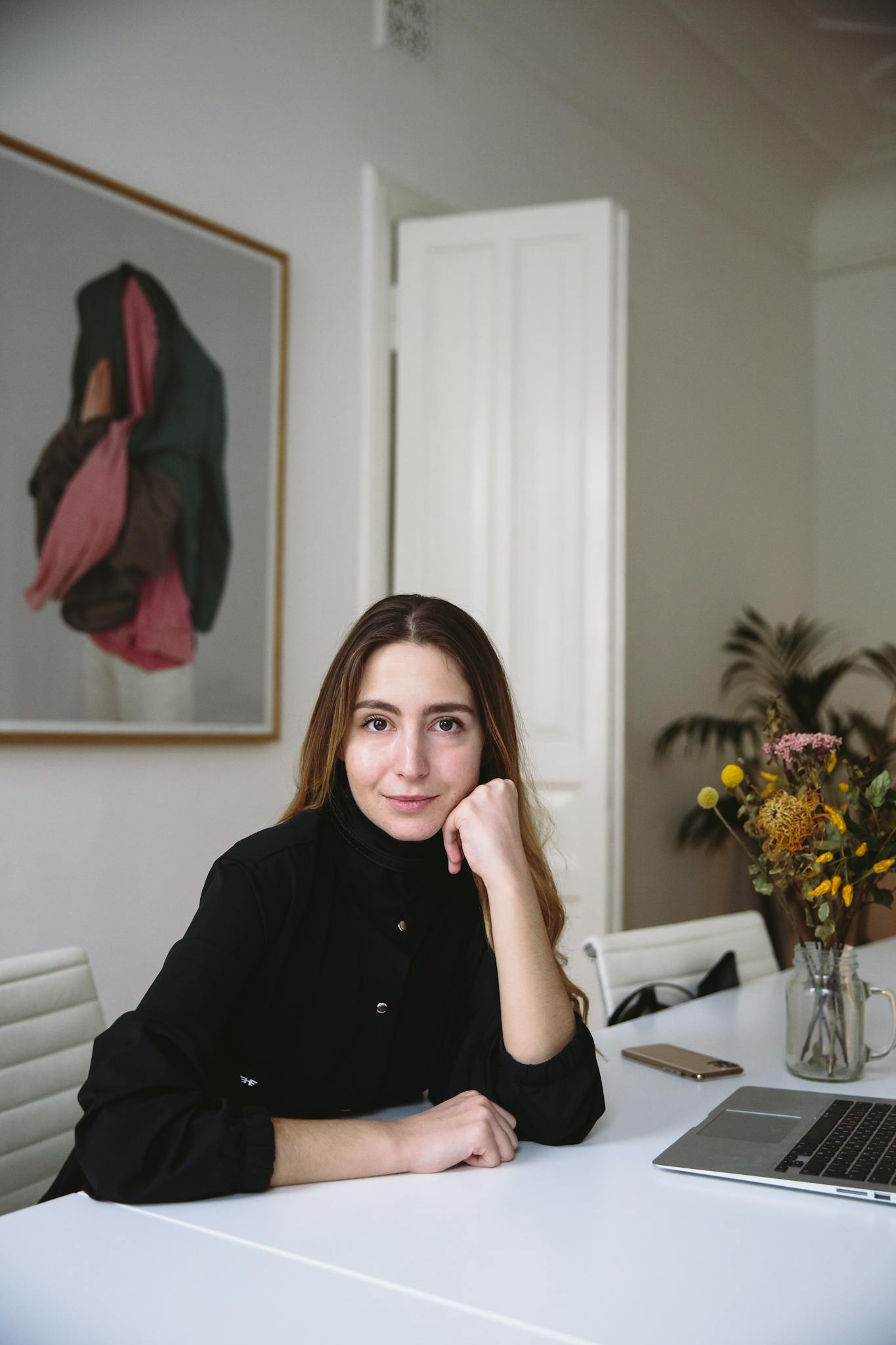 Portrait of a woman in a modern office setting, seated at a desk with a laptop.